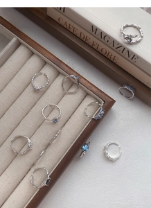 Dettaglio degli anelli in argento S925 con trama lava e zircone blu su vassoio beige