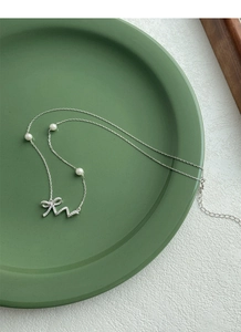 Detail of 925 silver necklace with bow pendant, zircon setting and three white pearls