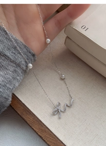 Close-up of a 925 silver bow necklace with sparkling crystals and white pearls on the chain