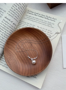 Dettaglio della collana in argento S925 con fiore e perla bianca su vassoio di legno
