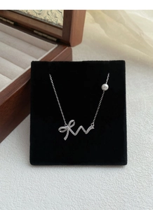 Detailed view of silver bow necklace with sparkling crystals and a single white pearl