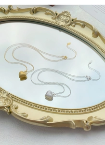 Close-up of gold and silver heart necklaces with matte texture on a vintage mirror