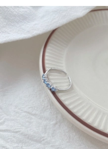 Dettaglio anello in argento con cinque zirconi blu chiaro su ceramica bianca