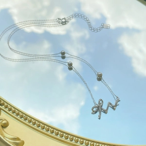 925 silver bow necklace with white pearl and diamonds reflecting blue sky on a mirror