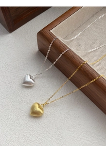 Detail of gold and silver heart necklaces with brushed matte texture on wooden tray
