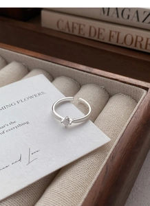 Detail shot of a silver square zircon ring with textured band in a wooden jewelry box