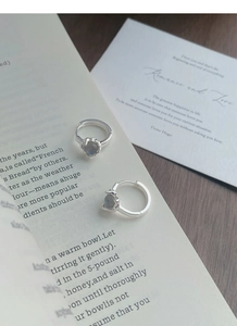 Macro detail of S925 sterling silver hoop earrings with heart-shaped moonstone on book