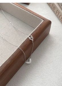 Close-up of S999 silver heart pendant and interlocking rings on a wooden tray