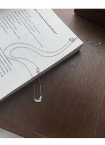 Macro detail of S999 sterling silver necklace with double-ring clasp and V-pendant on book