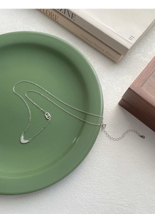 Detail of S999 silver heart necklace with interlocking rings on a green ceramic plate