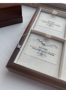 Macro shot of S925 silver clover bracelet with light blue cord in walnut jewelry box