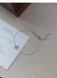 Close-up of light blue woven bracelet with silver clover pendant and adjustable clasp