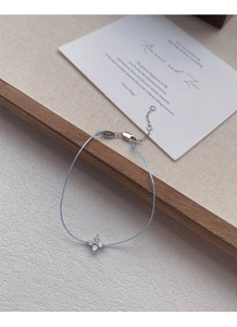 Detailed macro of S925 silver four-leaf clover pendant on light blue woven cord bracelet