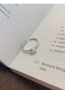 Close-up of adjustable S925 silver ring featuring a white oval freshwater pearl on a book