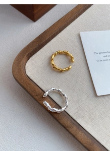 Detail view of twisted gold and silver S925 rings on a wooden tray with elegant textures