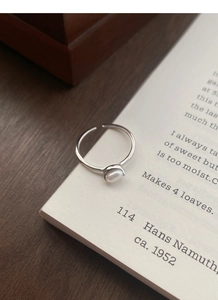 Detailed shot of an adjustable S925 silver ring with a natural pearl on an open book