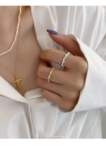 Detail of twisted silver and gold rings paired with pearl and cross pendant necklaces