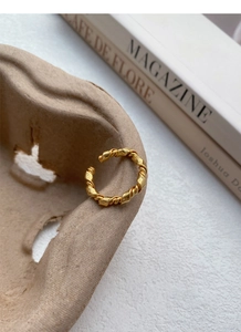 Detail shot of a minimalist gold twisted knot ring on a textured paper prop