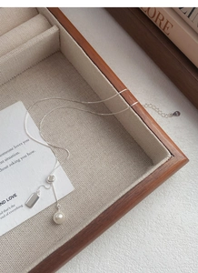 Detail of S925 sterling silver chain with a pearl and rectangular pendant on wood