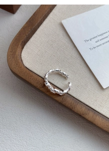 Close-up of S925 sterling silver knotted ring on a wooden tray with a canvas texture