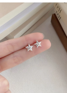 Détail de boucles d'oreilles étoiles en argent avec zircone et bordure perlée sur le doigt