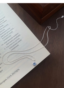 Vue détaillée d'un pendentif fleur en argent S925 avec zircon bleu sur un livre ouvert
