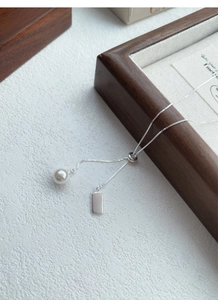 Detail of adjustable S925 silver chain with round white pearl and polished rectangle tag