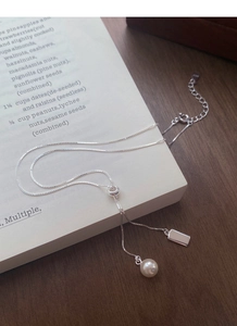 Close-up of S925 silver pearl necklace with rectangular charm on a book page