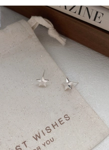 Détail macro de boucles d'oreilles étoile en argent S999 sur pochette en coton
