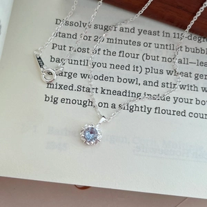 Collier en argent S925 avec pendentif fleur en zircon bleu sur une page de livre