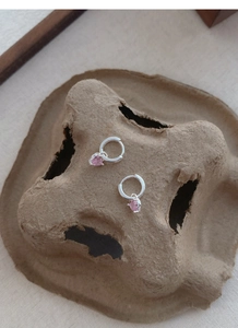 Détail de boucles d'oreilles en argent S999 avec pendentif cœur rose sur fond rustique