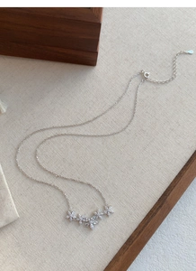 Dettaglio collana in argento S999 con cinque fiori e zirconi su tessuto beige caldo
