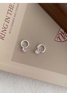 Détail des créoles cœur en argent S999 avec zircon rose posées sur un magazine