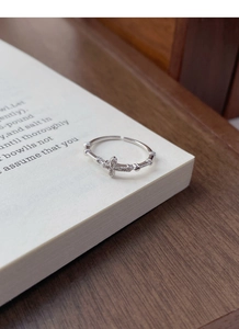 Macro view of adjustable silver cross ring featuring shimmering zircon stones on a book