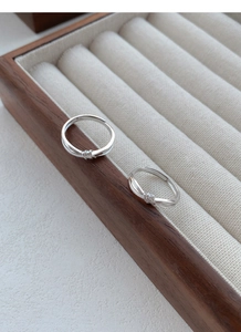 Dettaglio macro degli anelli a nodo in argento con diamanti pavé su espositore in noce