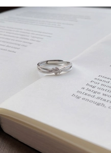 Dettaglio dell'anello a nodo in argento S999 con piccoli zirconi su pagine di libro