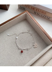 Macro detail of S925 silver double-layered bracelet with red agate bead and bear pendant
