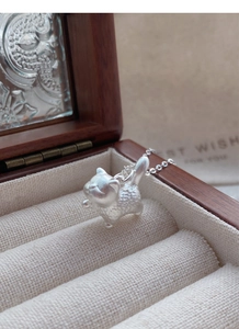 Detailed view of a 3D matte silver cat pendant resting on a dark wood jewelry box