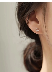 Gros plan d'une boucle d'oreille fleur évidée en argent S999 portée par un mannequin
