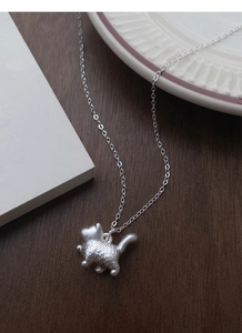 Detail of S999 silver cat pendant showing matte brushed texture on a wood surface