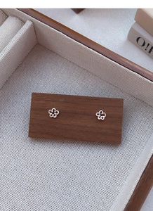 Détail de boucles d'oreilles fleurs en argent S999 sur un support en bois sombre