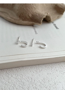 Makroansicht von S999 Silber Zirkonia Ohrsteckern und C-förmigen Creolen auf einem Buch