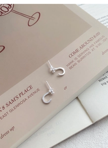 Detailansicht der silbernen S999-Ohrstecker mit weißem Zirkon auf Magazin-Hintergrund
