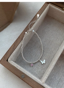 Détail macro du bracelet perlé en argent S925 avec étoile rose et breloque papillon blanc
