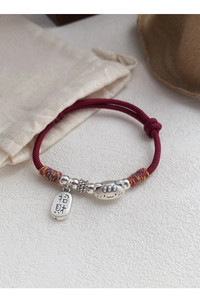 Détail du bracelet en soie rouge fait main avec chat porte-bonheur en argent et breloques