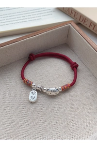 Détail du charm chat en argent S999 et pendentif porte-bonheur sur bracelet tressé rouge