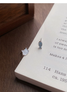 Details von asymmetrischen Katzen- und blauen Fischohrsteckern aus S999-Silber auf einem Buch