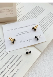 Macro detail of bow-shaped silver earrings with black heart-shaped zircons on card