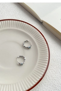 Détail de créoles en maillons argentés avec pierres carrées bleues sur plateau céramique