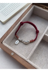 Détail du bracelet tressé rouge avec pendentif chat en argent et breloque porte-bonheur